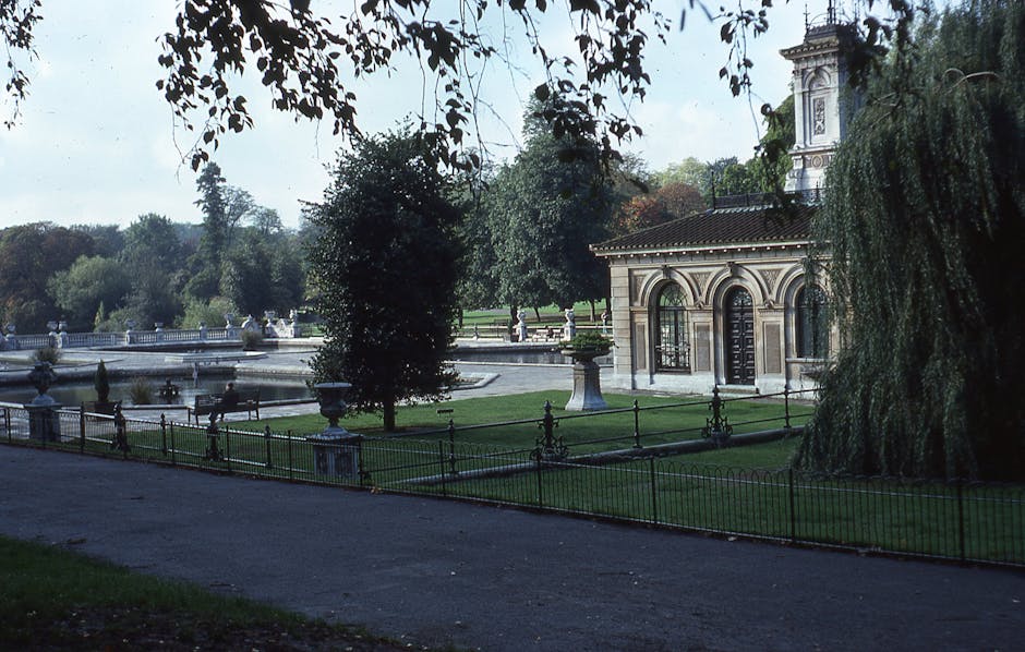 A stone-built viaduct with multiple arches stretches across a garden scene. The arches are constructed from a combination of bricks and flint stones, showing evidence of weathering and age. To the rig